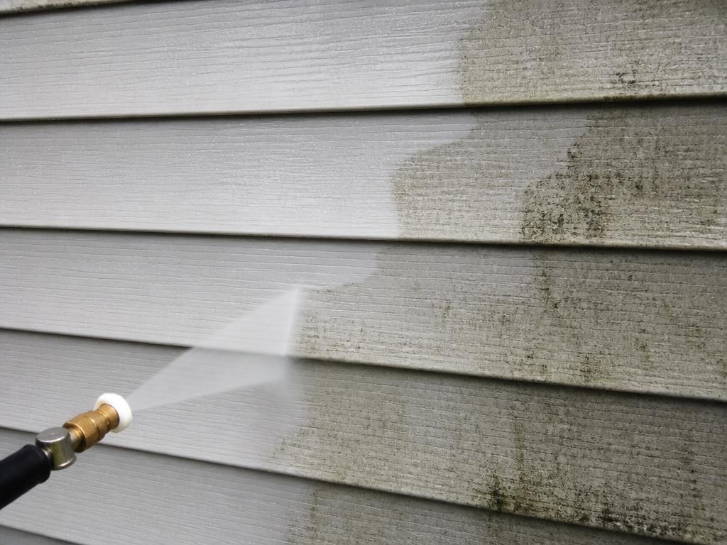 Pressure washer nozzle cleaning mildew from gray vinyl house siding