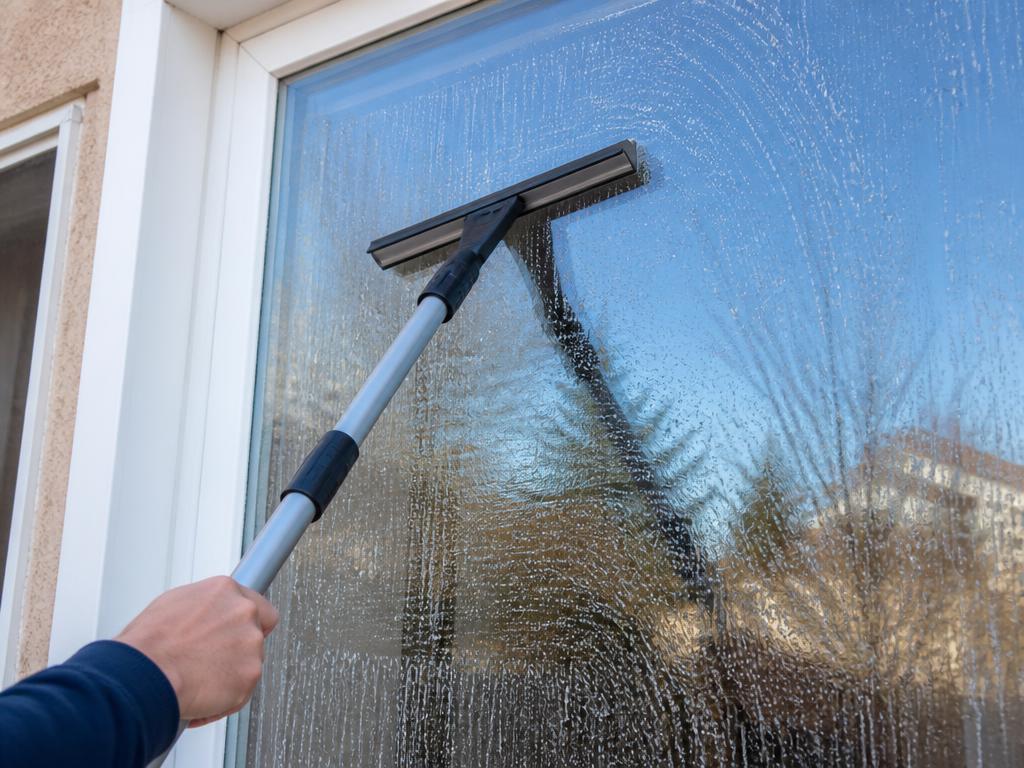 Squeegee wiping soapy water off an exterior residential window